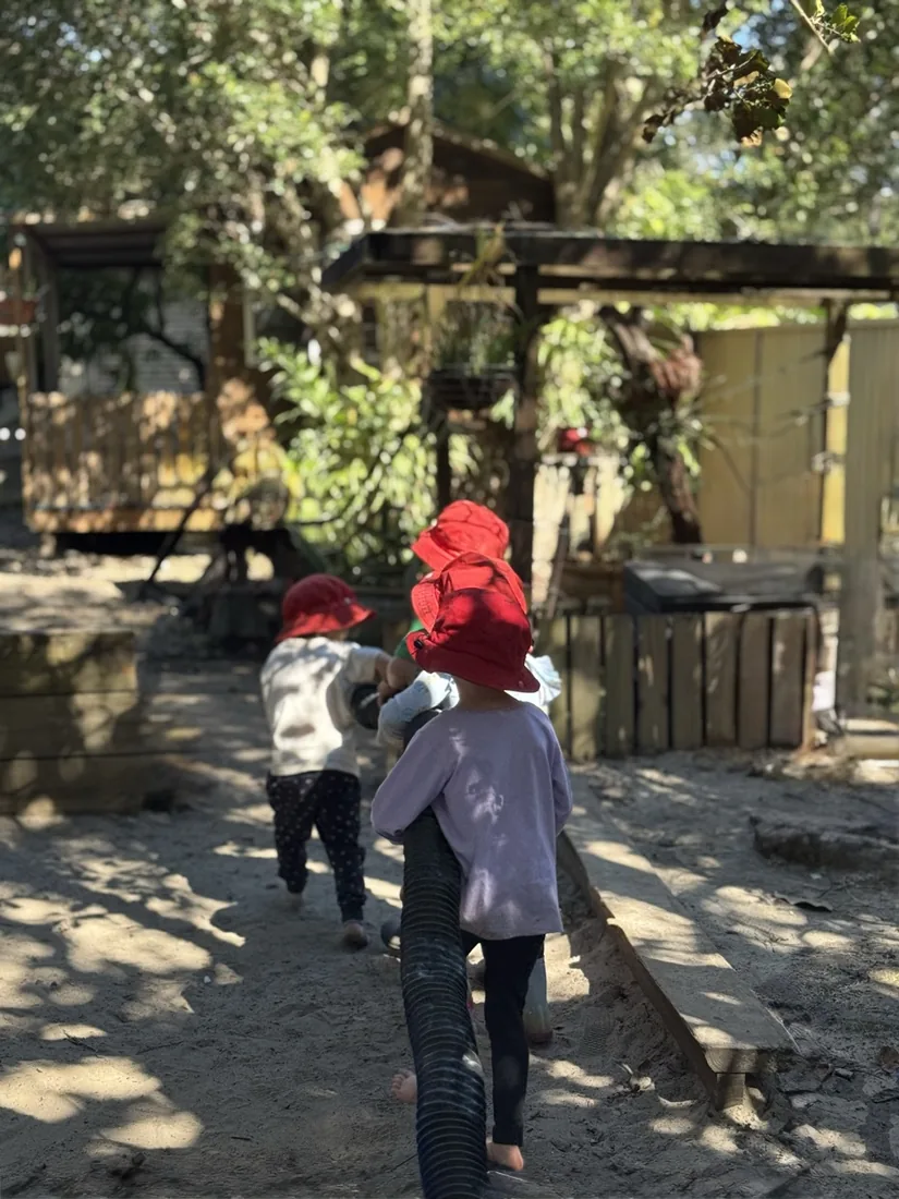 Two children carrying a long tube through the sandpit